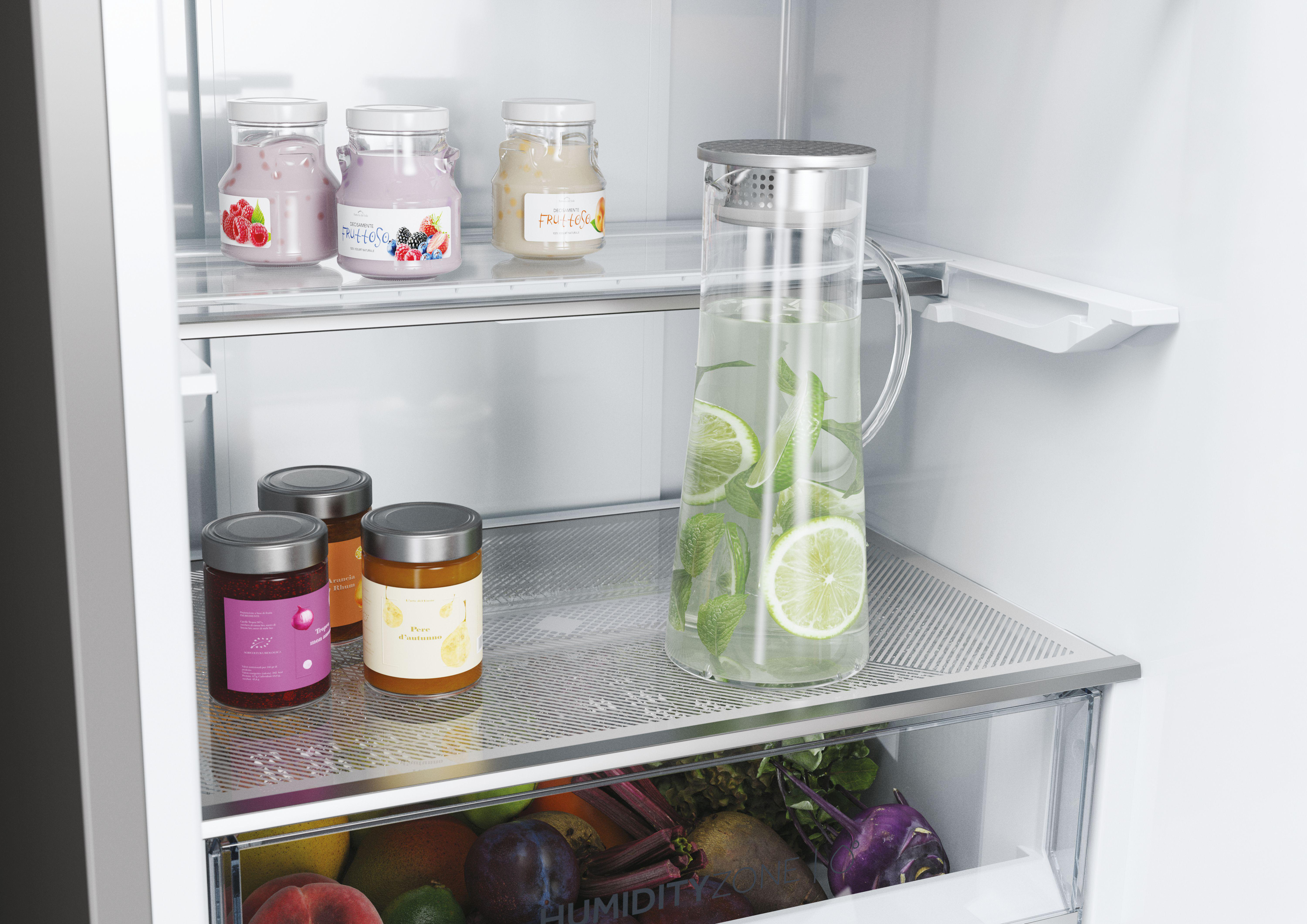 Kühlschrank-Innenraum mit Marmeladengläsern, Wasserkrug mit Limettenscheiben und Gemüse.