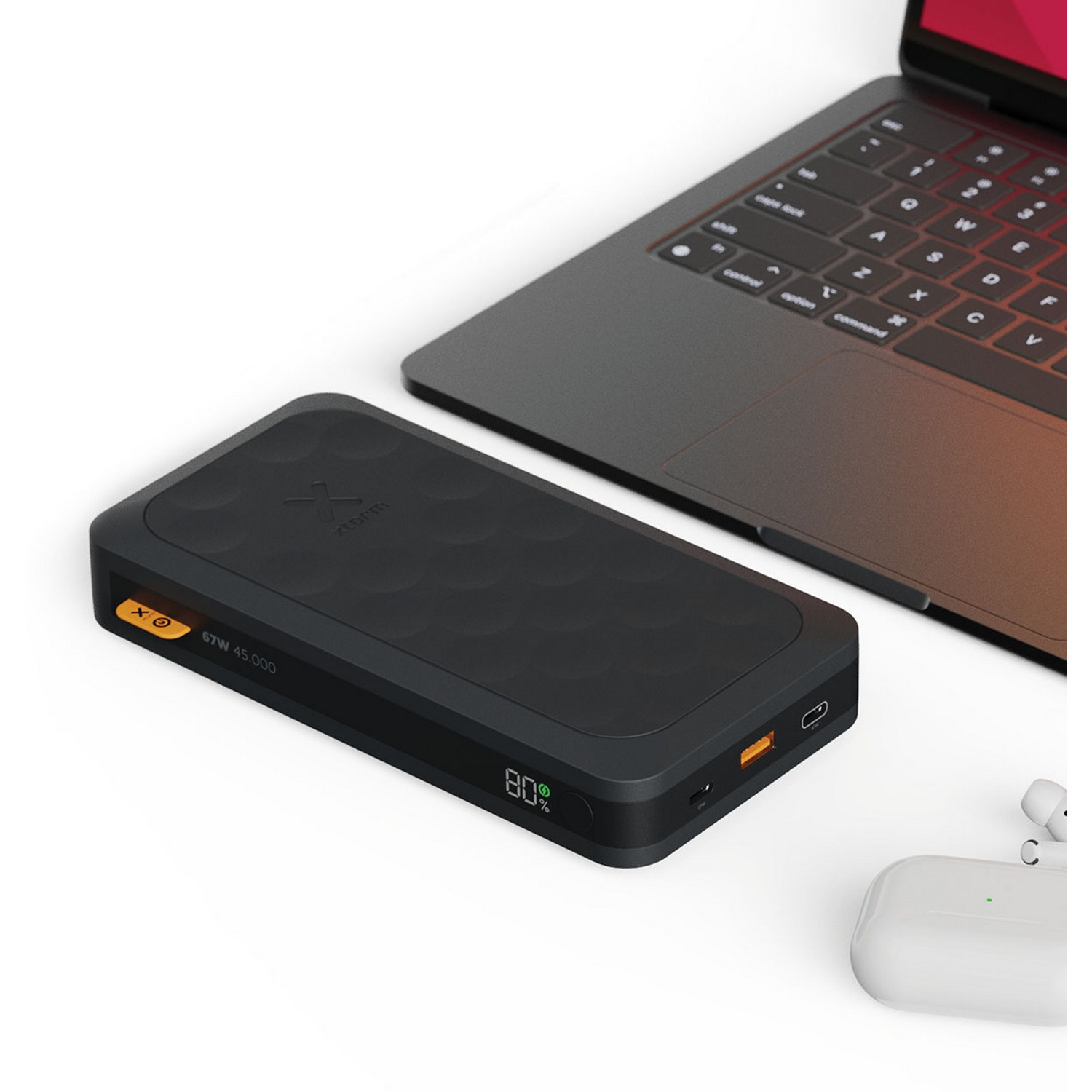 A black power bank with a laptop, wireless earbuds, and a charging cable on a white surface.