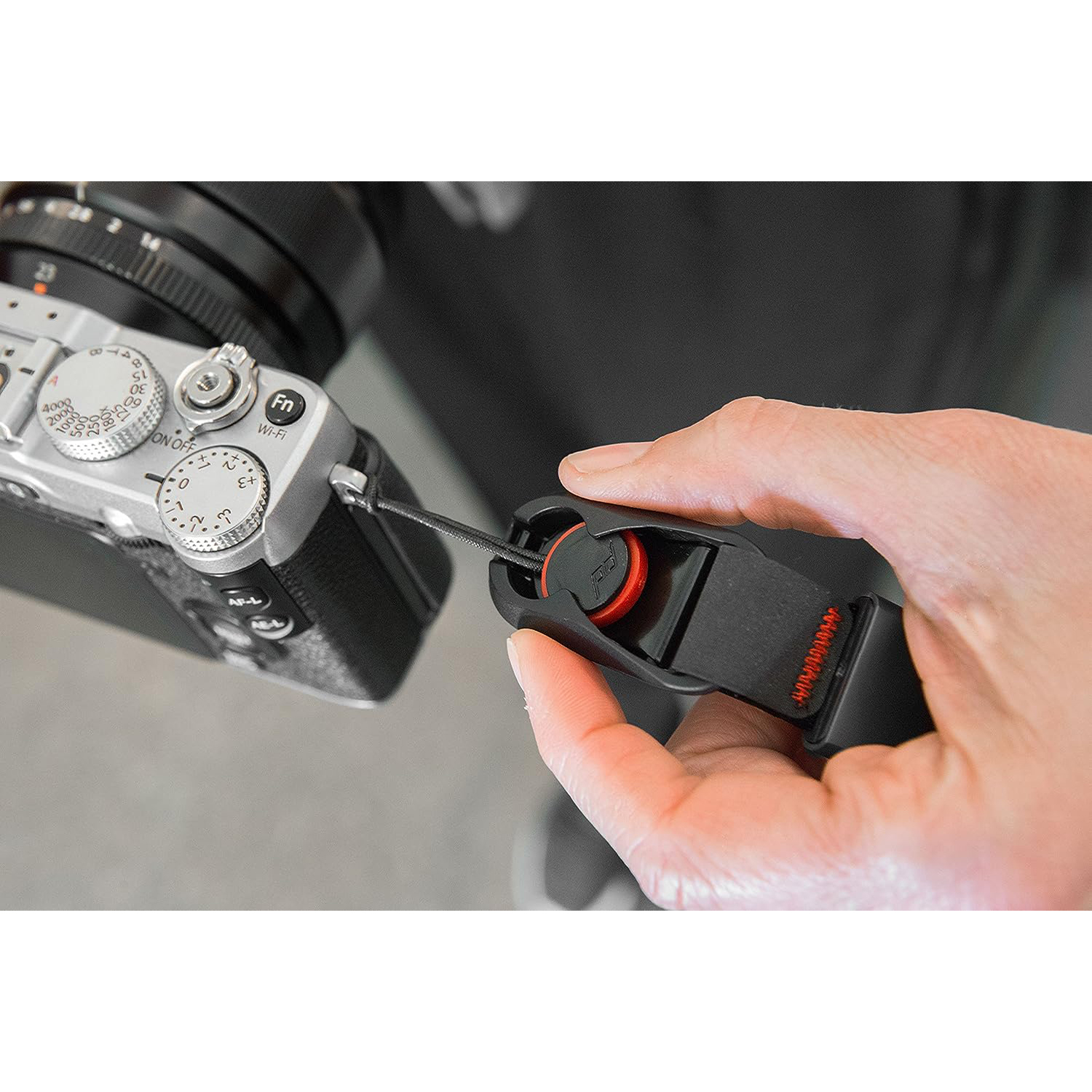La mano di una persona che tiene un cinturino nero con un pulsante rosso e una fotocamera.
