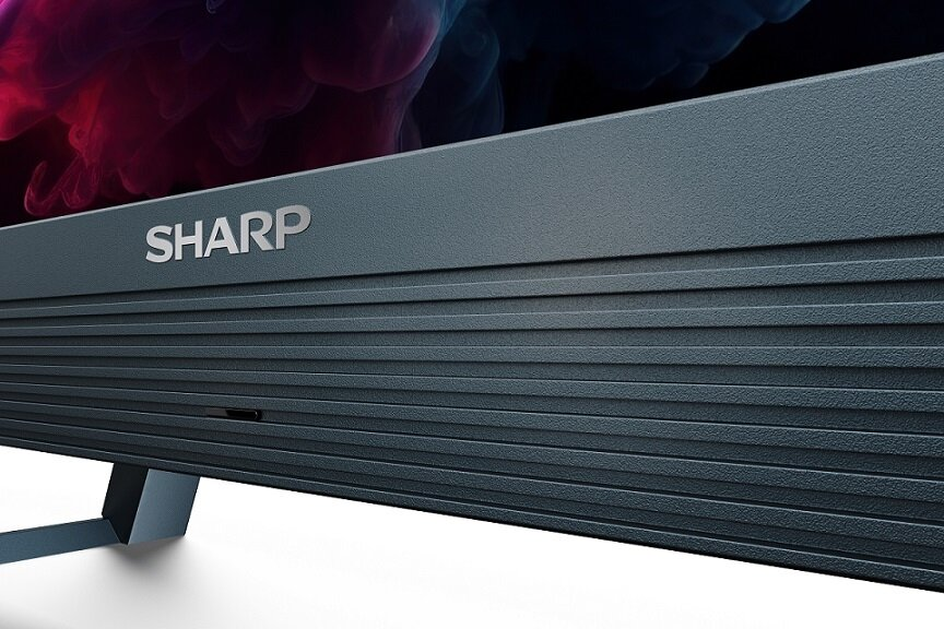 Zbliżenie telewizora Sharp. Logo jest na górze. Dół ma ciemny, żebrowany wzór.