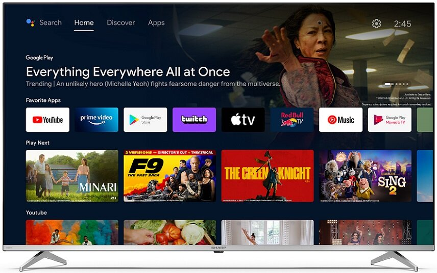 Telewizor Sharp wyświetlający ekran główny z ikonami filmów i aplikacji, na białym stojaku.