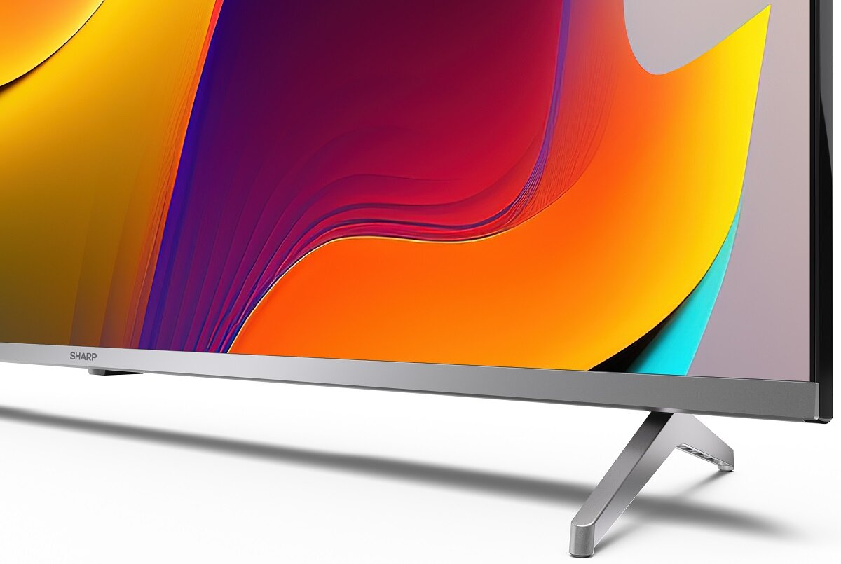Zbliżenie na telewizor. Srebrna podstawa i kolorowy ekran. Wyświetla kolory pomarańczowy, fioletowy i żółty.