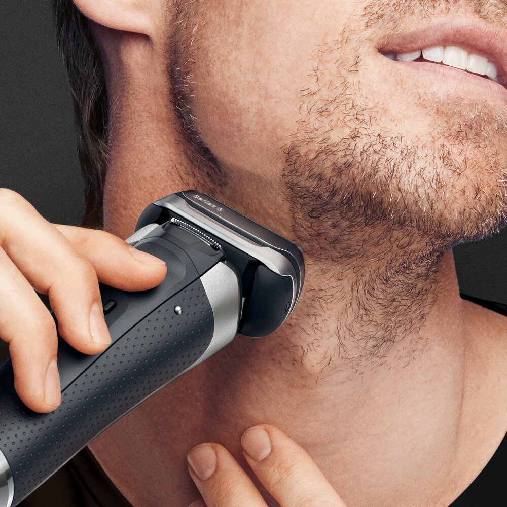 Mężczyzna goli brodę czarno-srebrną golarką elektryczną, zbliżenie.