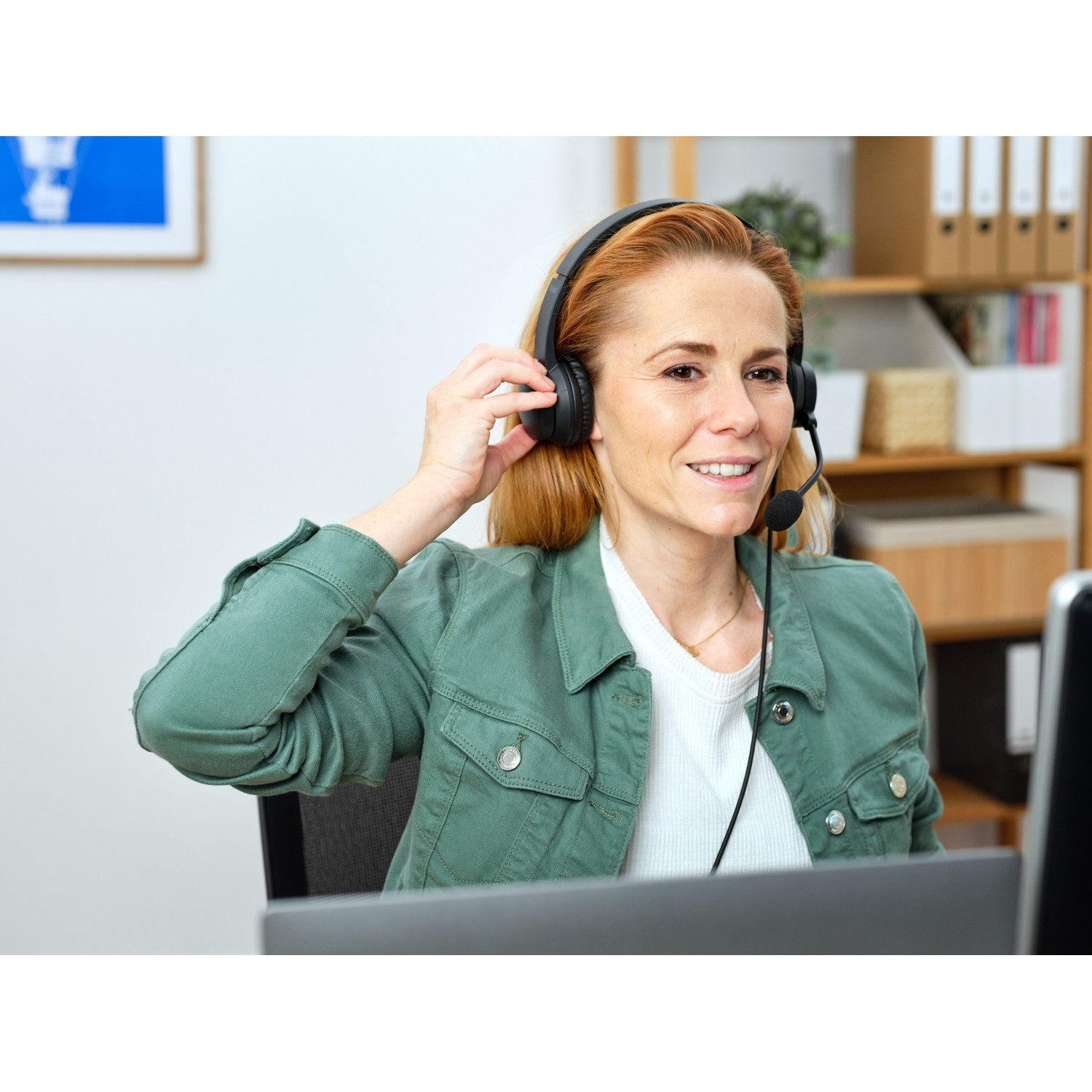 Woman wearing a black headset with a microphone, smiling at a computer screen.