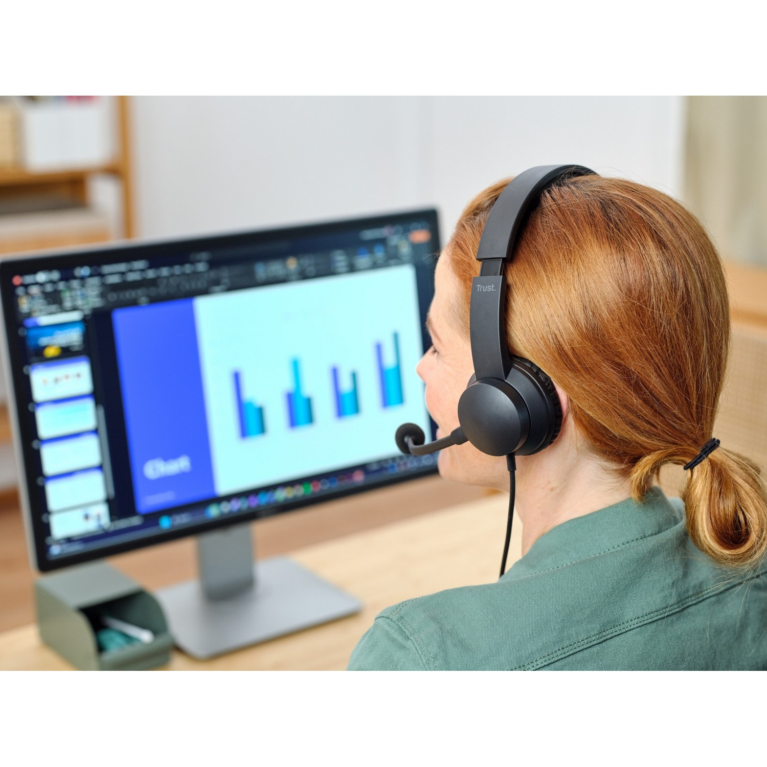 A woman with a headset looks at a computer monitor displaying charts and graphs.