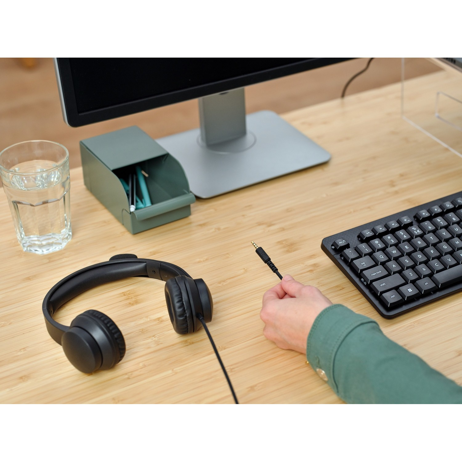 A desk with a glass of water, a pen holder, headphones, and a keyboard.