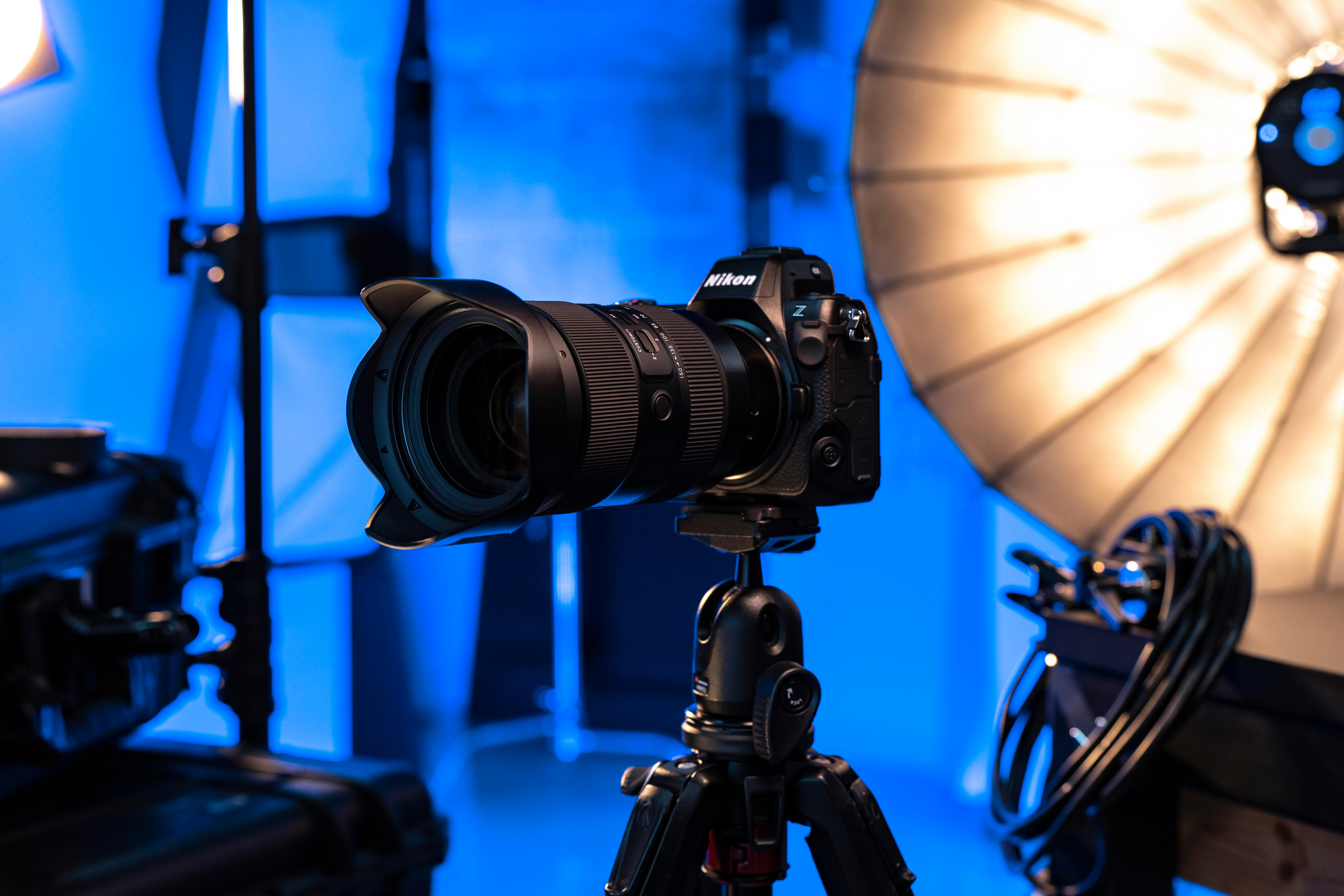 Eine Nikon-Kamera mit Objektiv auf einem Stativ. Der Hintergrund zeigt Studiolichter und blaue Paneele.