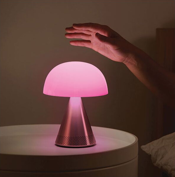 Ręka sięga do różowej lampy w kształcie grzyba na białym stole.