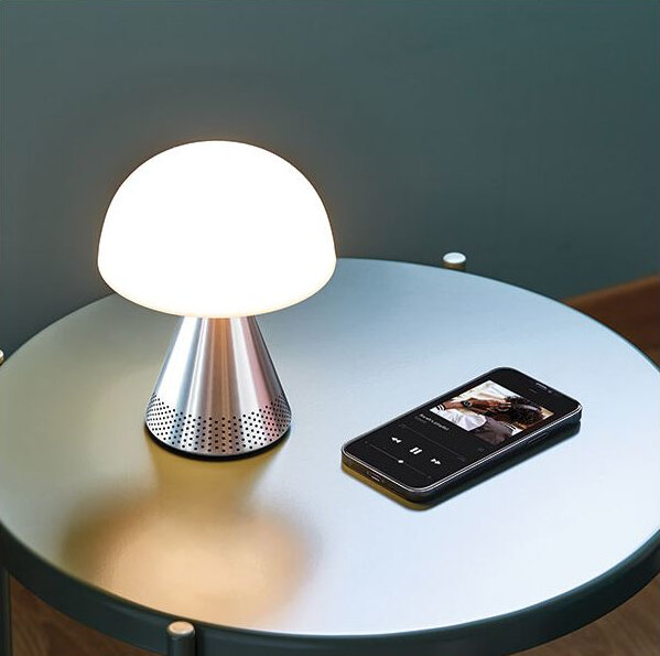 Lampa w kształcie grzyba na stole obok czarnego smartfona odtwarzającego muzykę.