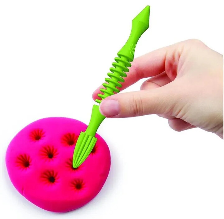 Ręka używa zielonego narzędzia do robienia dziur w różowej glinie.