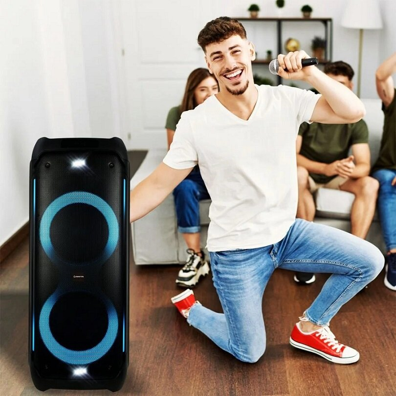 Mężczyzna śpiewa do mikrofonu, klęczy obok głośnika. Przyjaciele w tle.