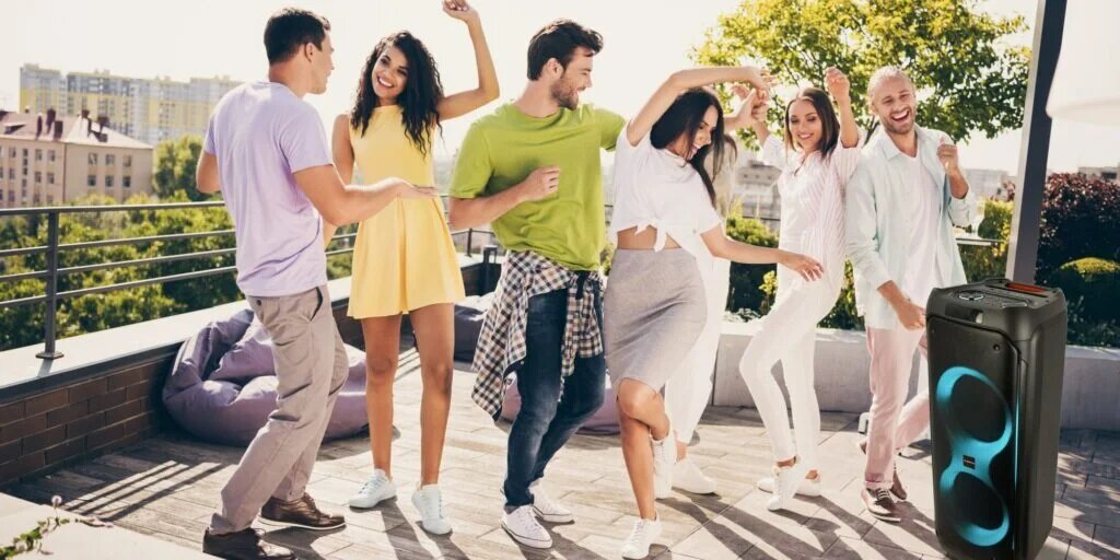Grupa ludzi tańczących na zewnątrz, obok dużego czarnego głośnika.