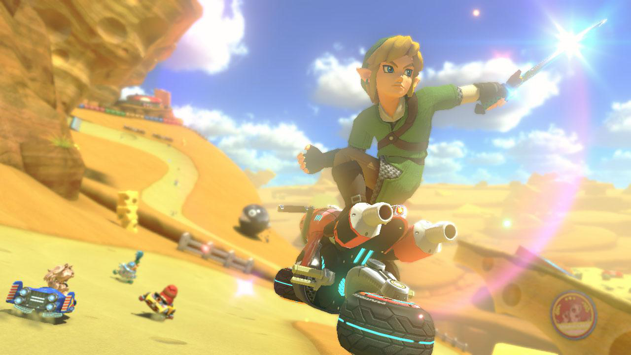 Link aus Zelda auf einem Hoverbike in einer Wüstenumgebung. Im Hintergrund Sanddünen und Felsen.