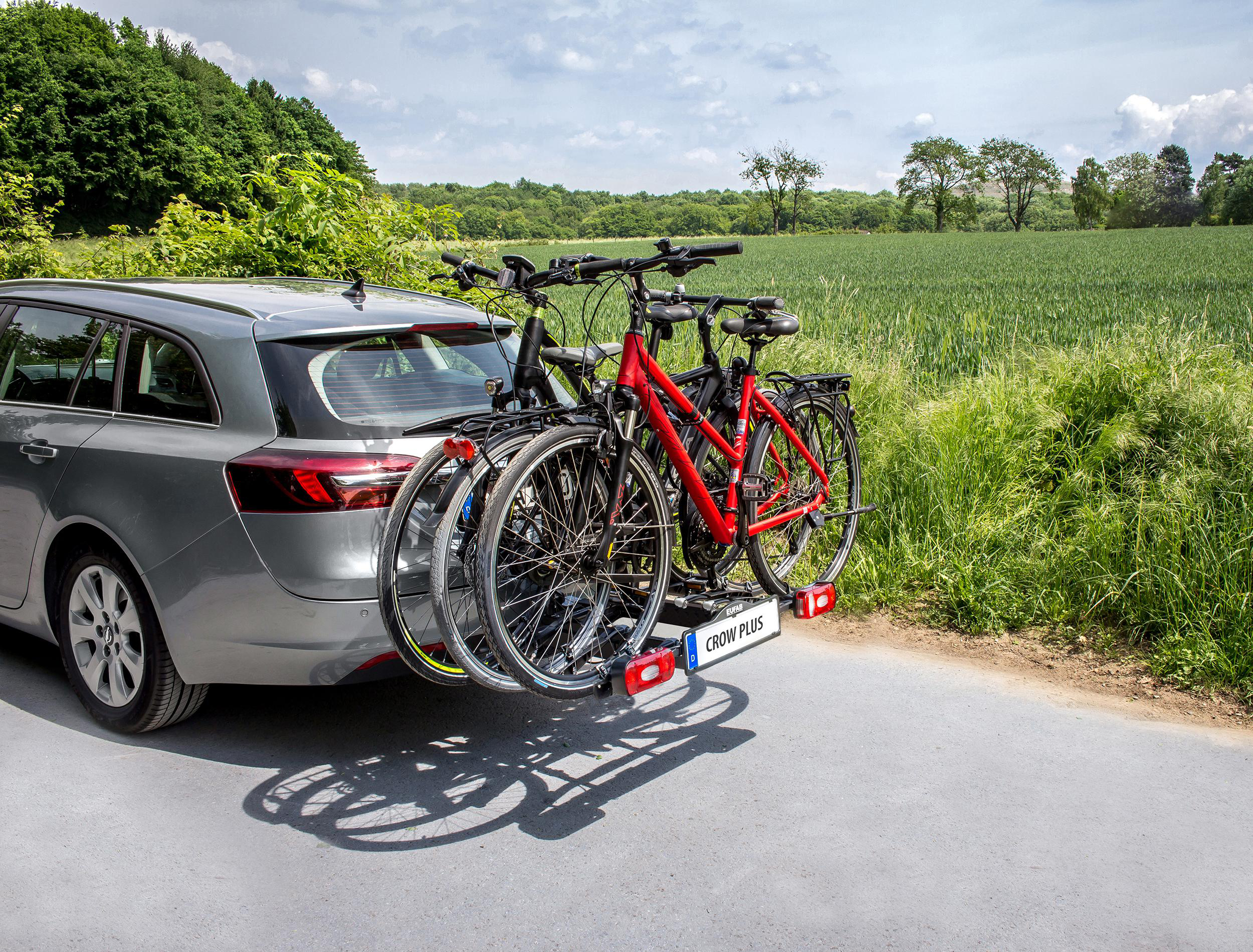 Ein silbernes Auto mit Fahrradträger, der 3 Fahrräder transportiert, parkt auf einer Straße.