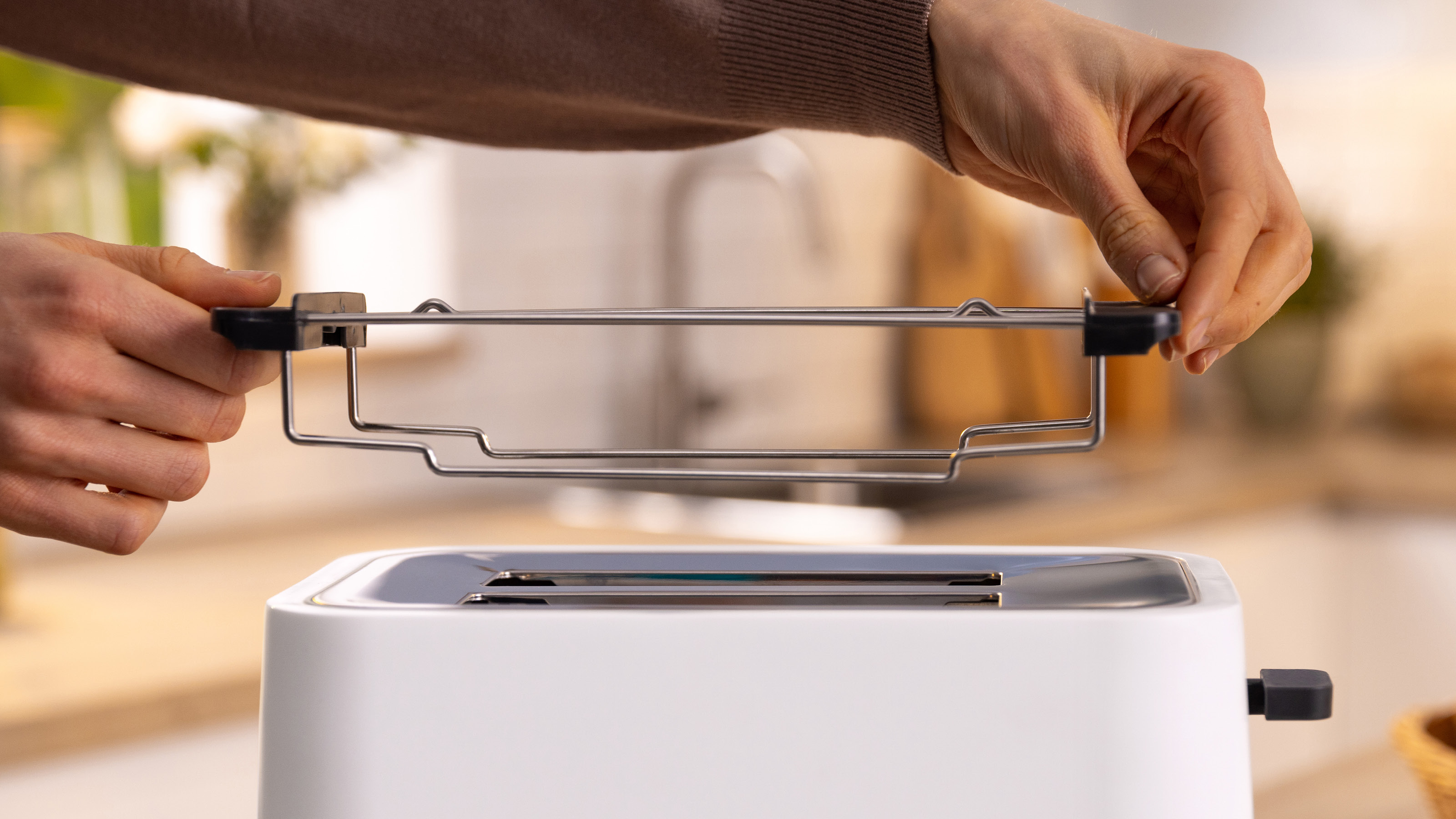 Hände, die einen Toaster in einen weißen Toaster einsetzen. Der Toaster ist silberfarben.