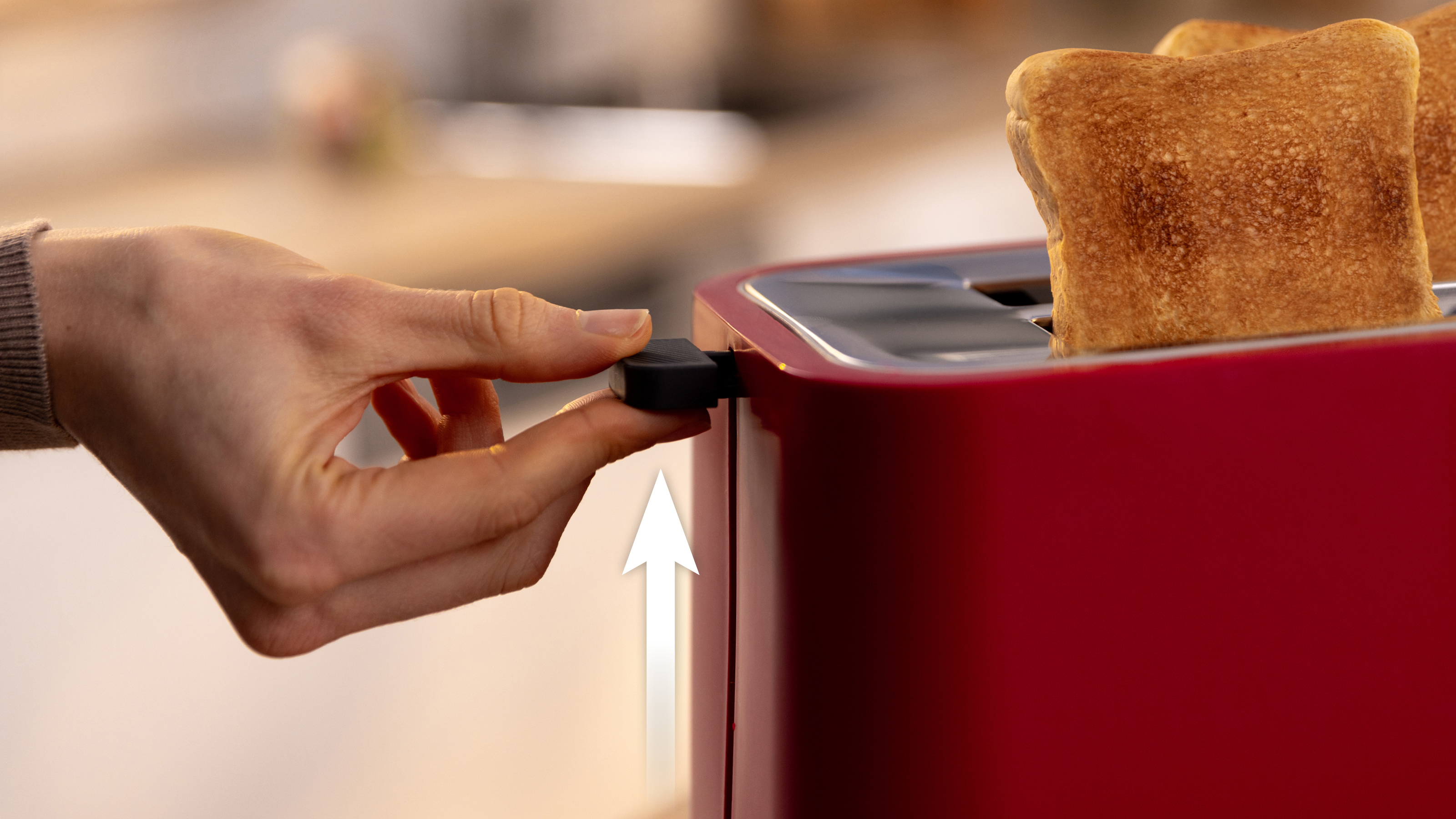 Hand hebt Hebel an rotem Toaster an, mit zwei Toastscheiben darin.