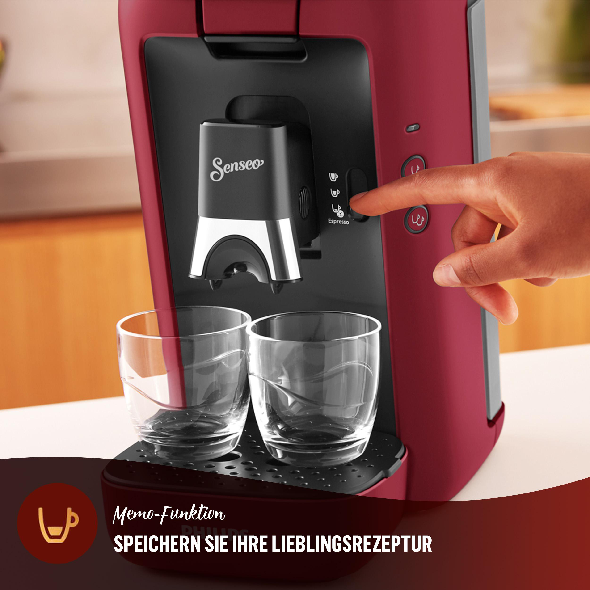 Rote und schwarze Kaffeemaschine mit zwei Gläsern. Eine Hand drückt einen Knopf.