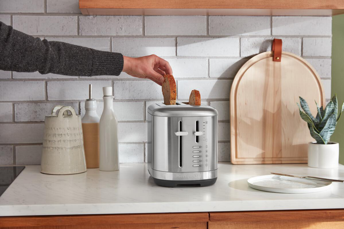 Hand legt Brot in einen silbernen Toaster auf einer Küchentheke.