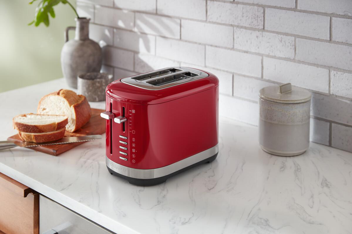 Roter Toaster auf einer weißen Arbeitsplatte. Brot und ein Glas stehen daneben.