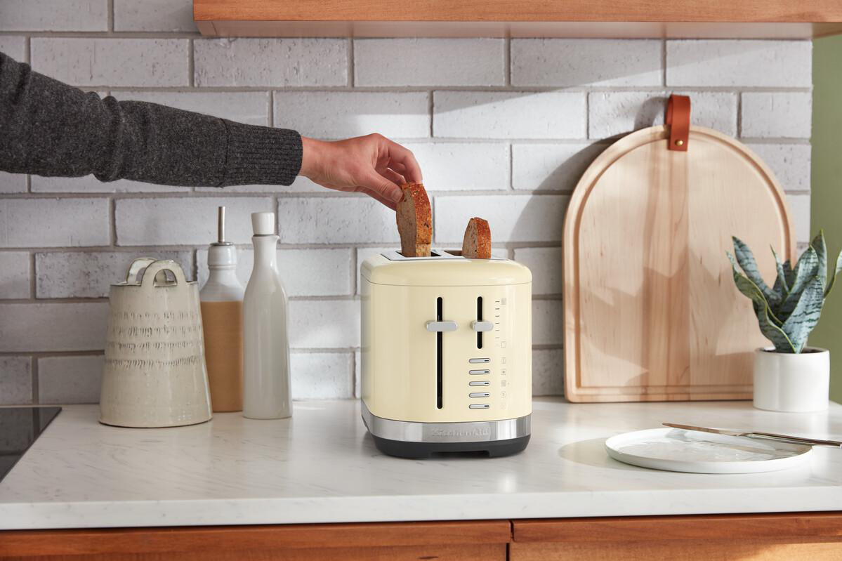 Eine Hand legt Brot in einen cremefarbenen Toaster auf einer Küchentheke.