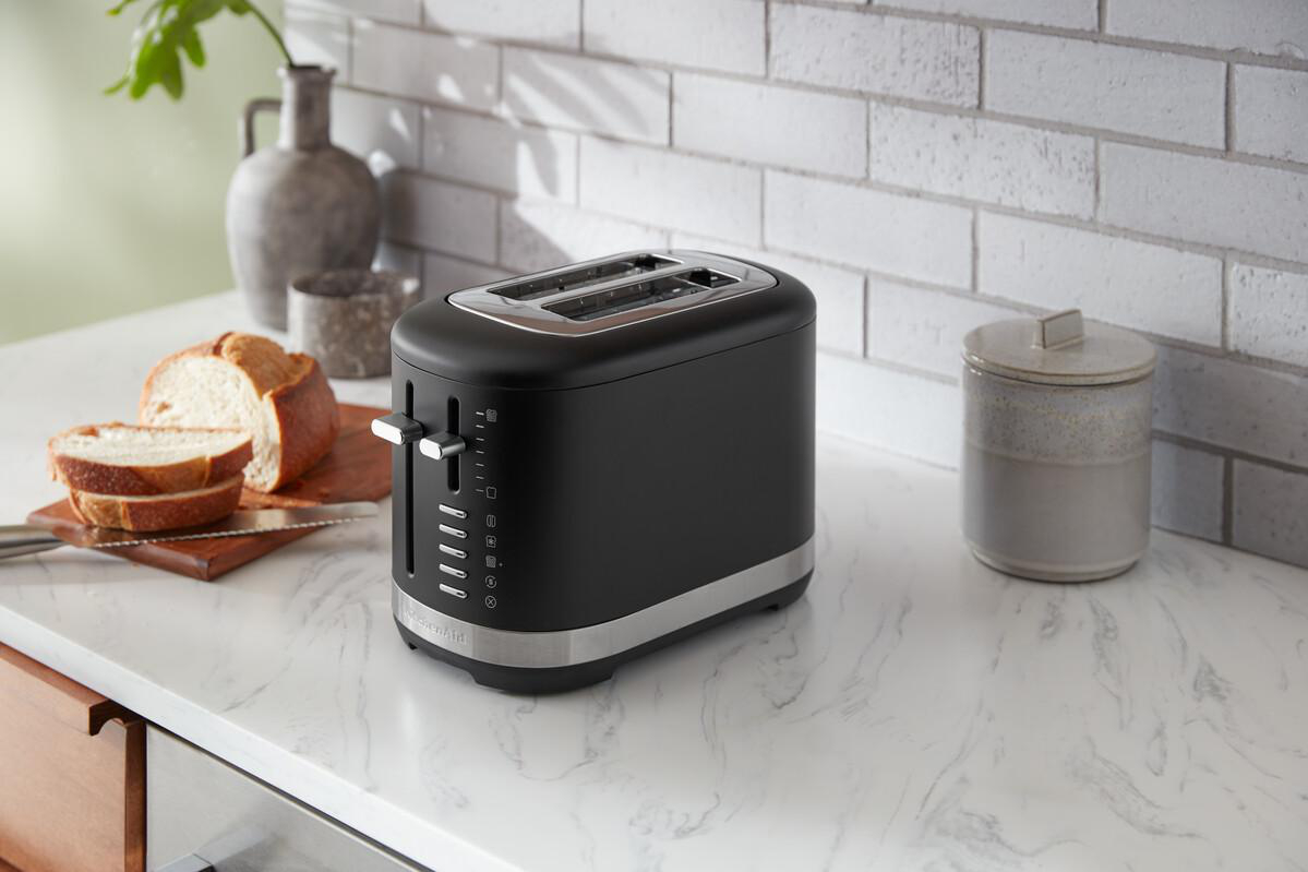 Ein schwarzer KitchenAid-Toaster mit Brot und anderen Gegenständen auf einer weißen Theke.