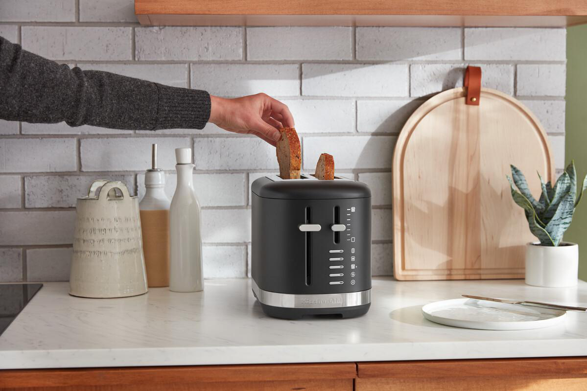 Eine Person nimmt eine Toastscheibe aus einem schwarzen Toaster.