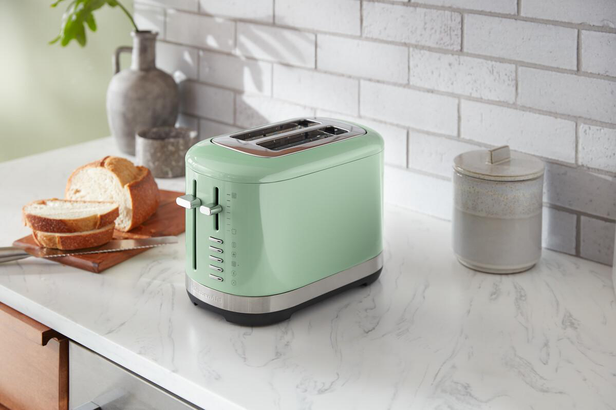 Ein mintgrüner Toaster auf einer weißen Arbeitsplatte mit geschnittenem Brot und einem Glas.