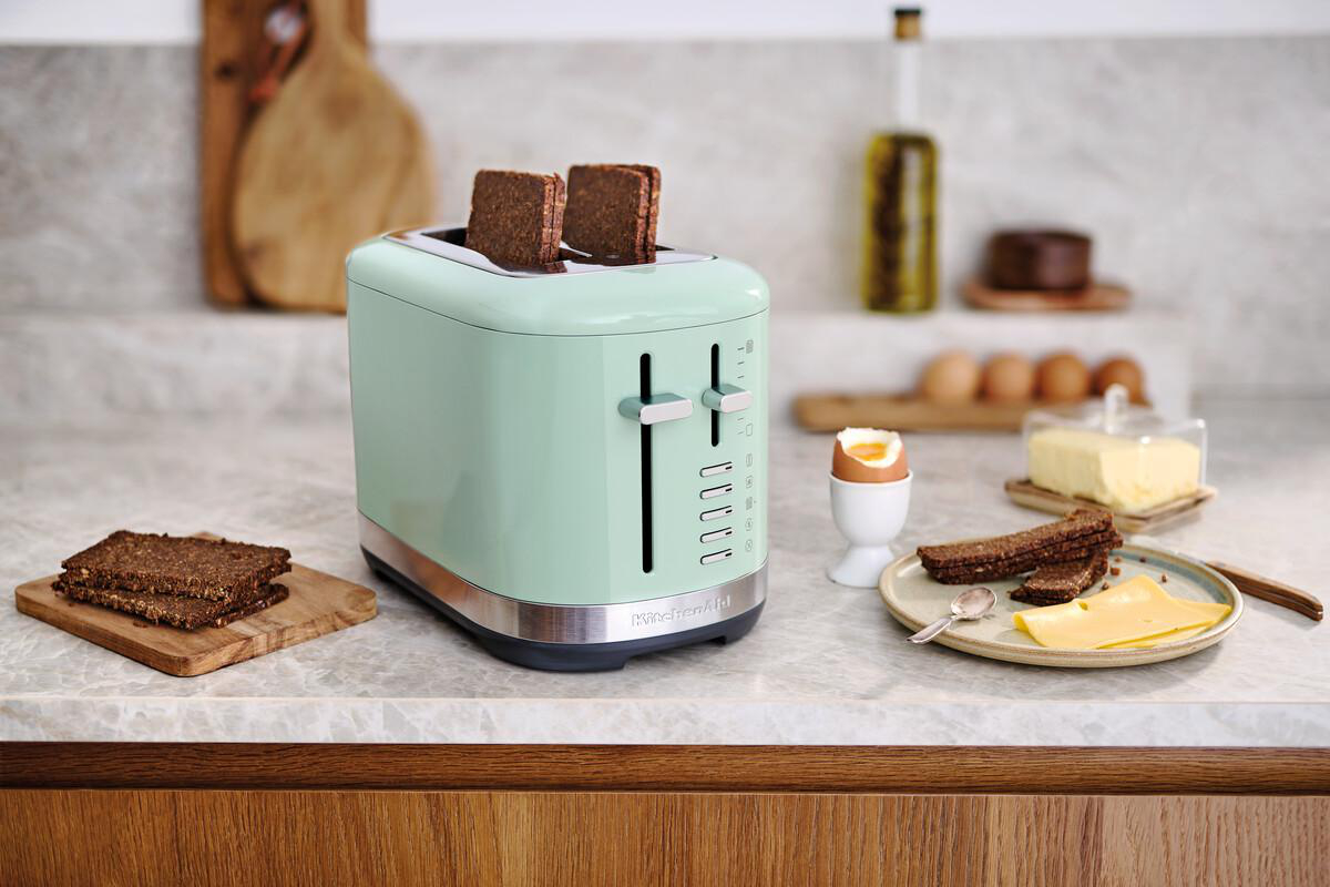 Minzgrüner Toaster mit Brotscheiben, Butter und gekochtem Ei auf der Arbeitsplatte.