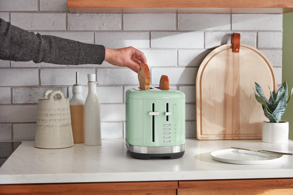 Eine Person, die Brot in einem mintgrünen Toaster auf einer weißen Theke toastet.