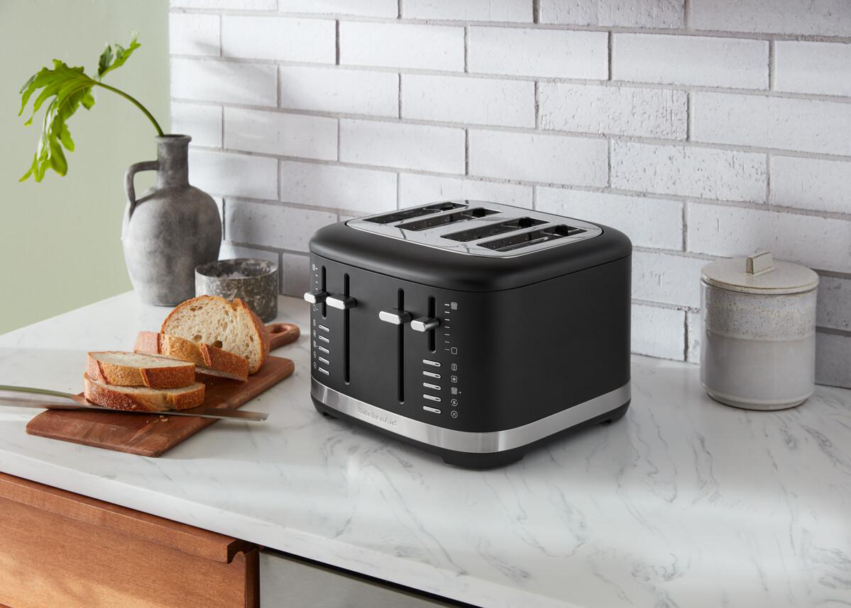 Schwarzer Toaster auf weißer Arbeitsplatte. Geschnittenes Brot und eine Pflanze in einer Vase stehen da.