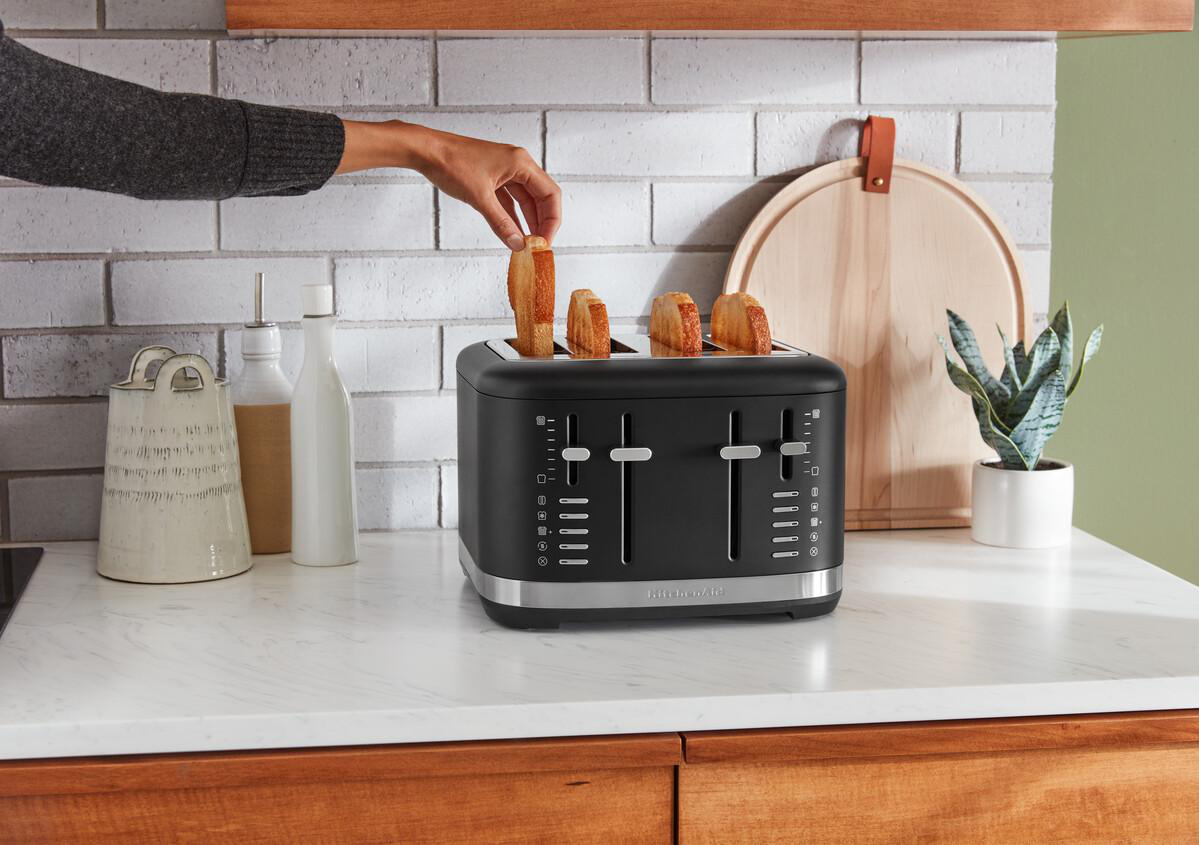 Die Hand einer Person, die Toast in einen schwarzen KitchenAid-Toaster für vier Scheiben auf einer Theke legt.