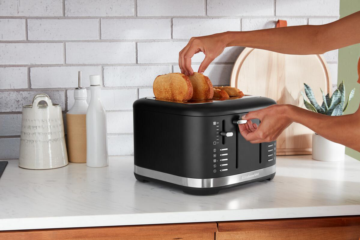 Hände legen Toast in einen schwarzen KitchenAid Toaster auf eine Küchentheke.