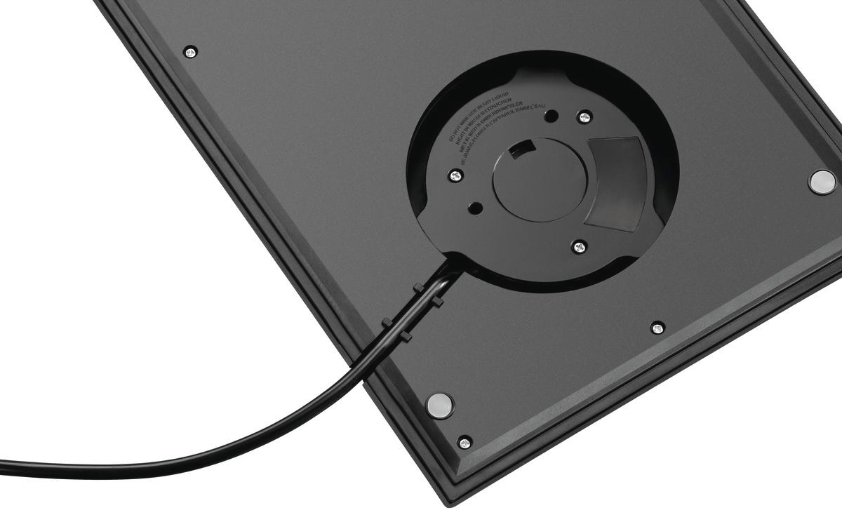 Nahaufnahme eines schwarzen, rechteckigen Geräts mit kreisförmiger Öffnung. Ein schwarzes Kabel ist angeschlossen. Schrauben sind sichtbar.