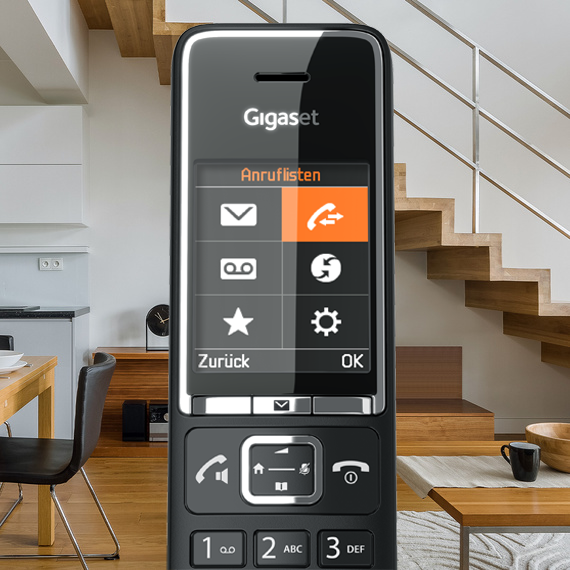 Egy fekete Gigaset telefon, a képernyőjén hívási beállításokkal. A háttérben egy nappali látható lépcsővel.