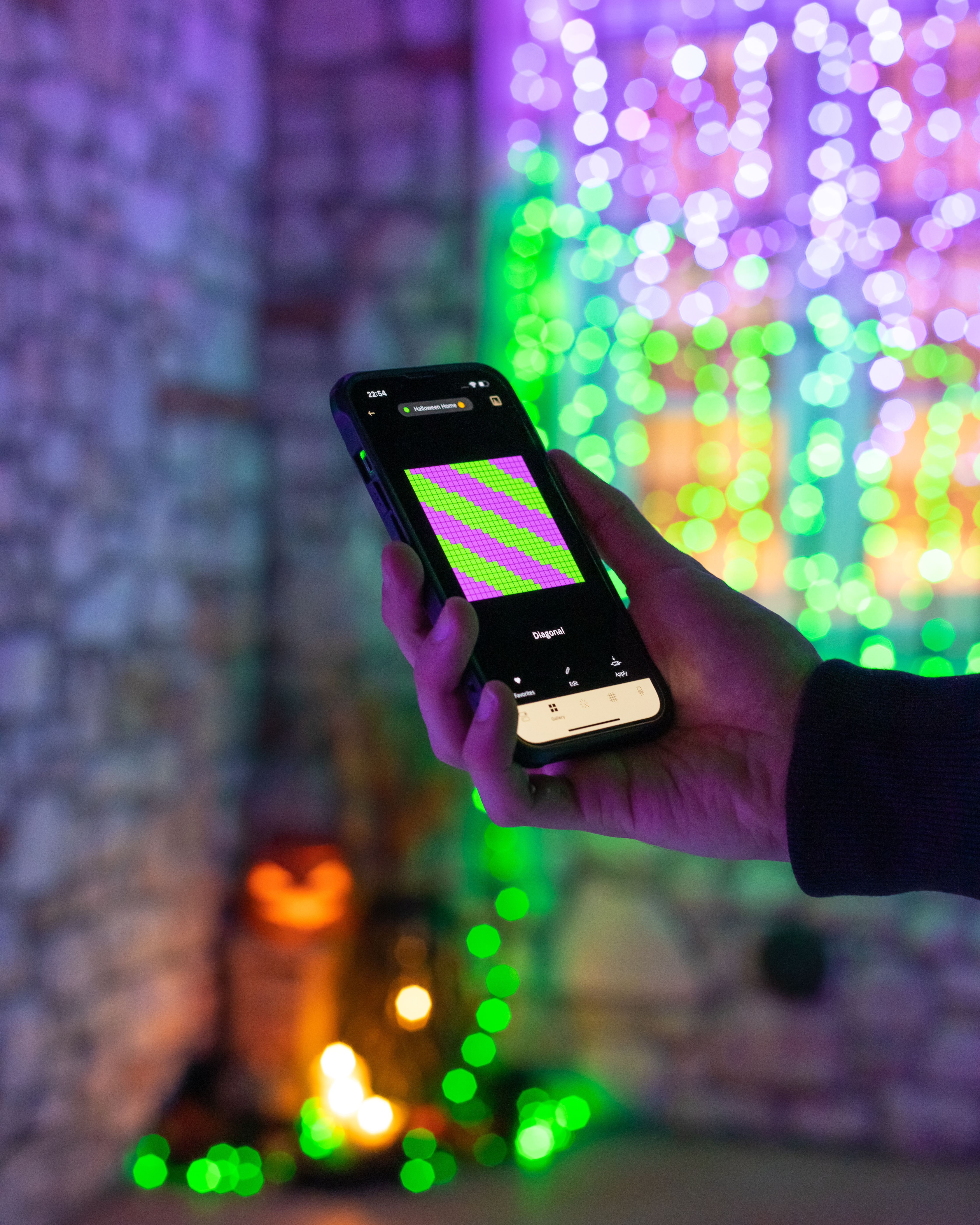 Hand hält Smartphone mit lila-grünem Muster vor bunten Lichtern.