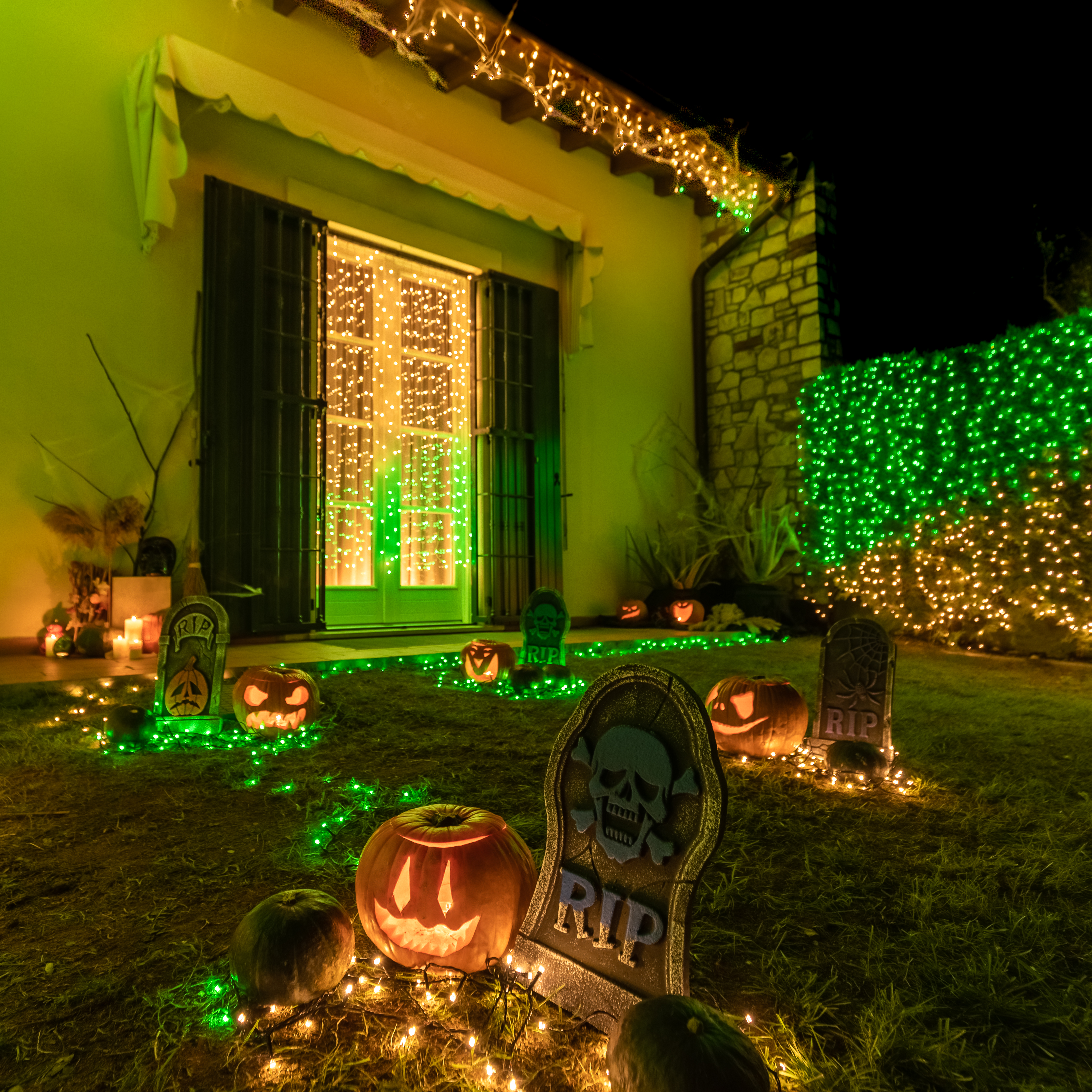 Nachtszenario, Halloween-Dekorationen. Kürbisse, Grabsteine, Lichterketten und ein Haus.