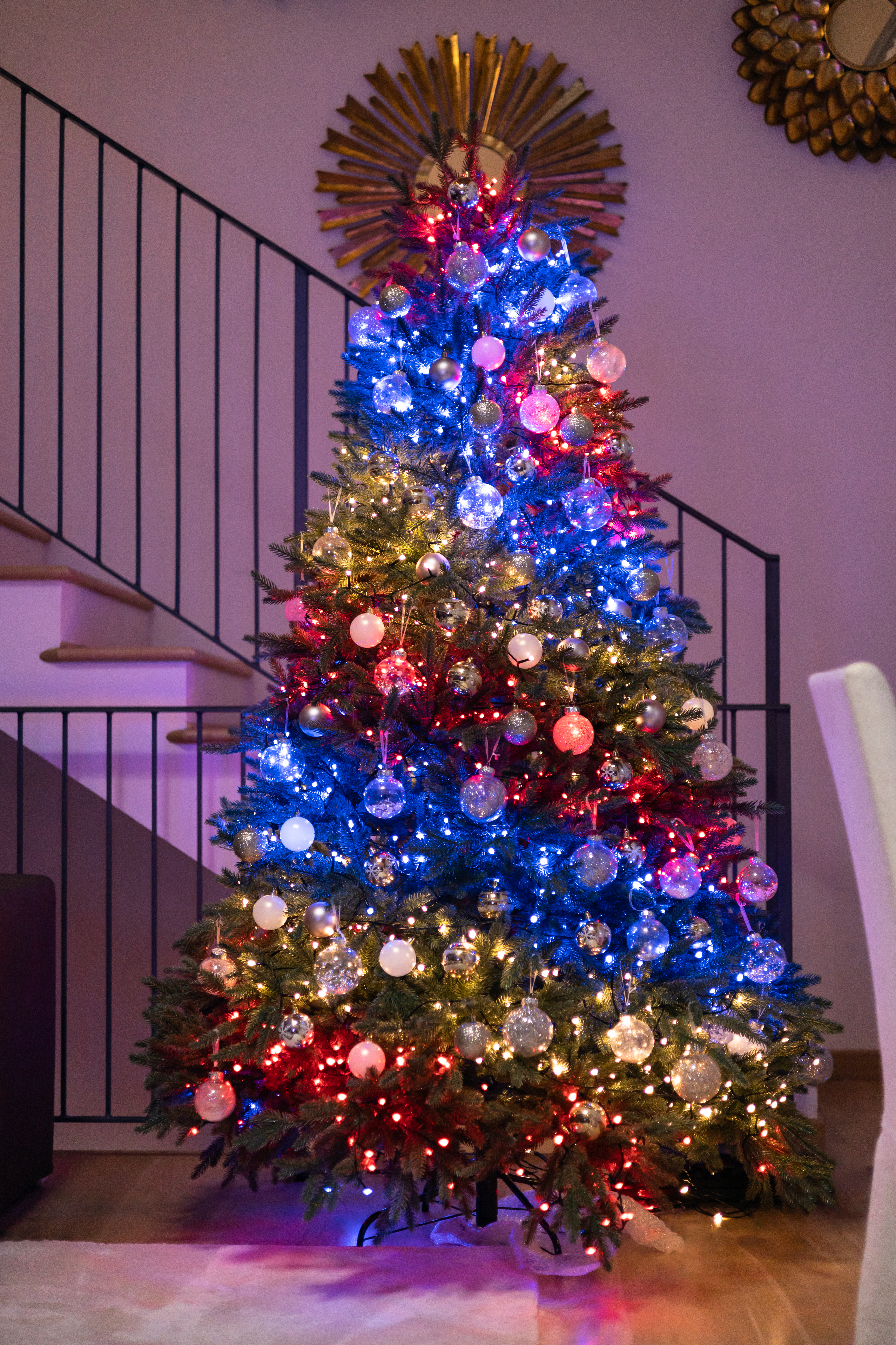 Ein geschmückter Weihnachtsbaum mit Lichtern und Ornamenten, in einem Wohnzimmer.