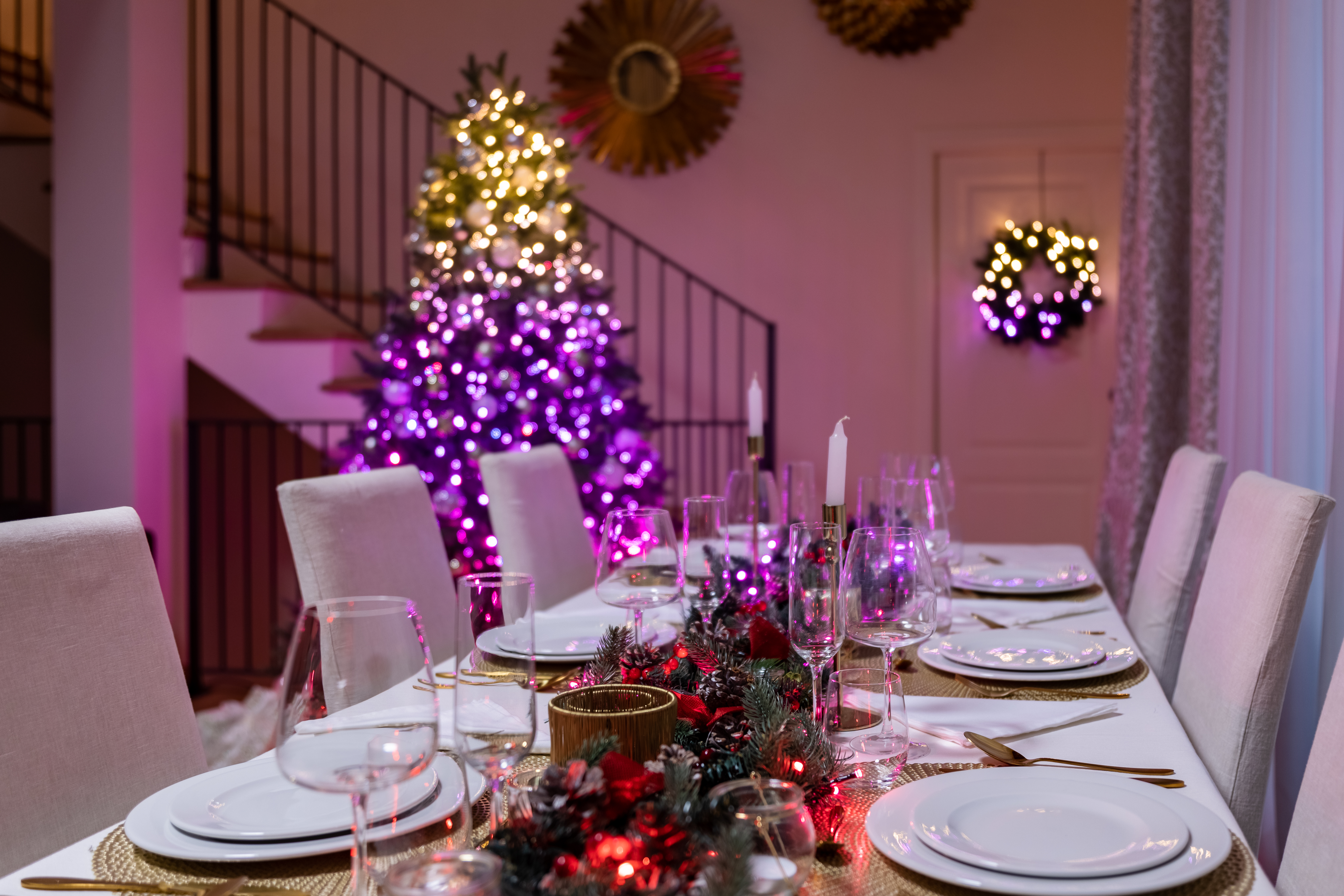 Festlich gedeckter Esstisch mit weißen Tellern, Kerzen und Weihnachtsbaum im Hintergrund, warme Atmosphäre.