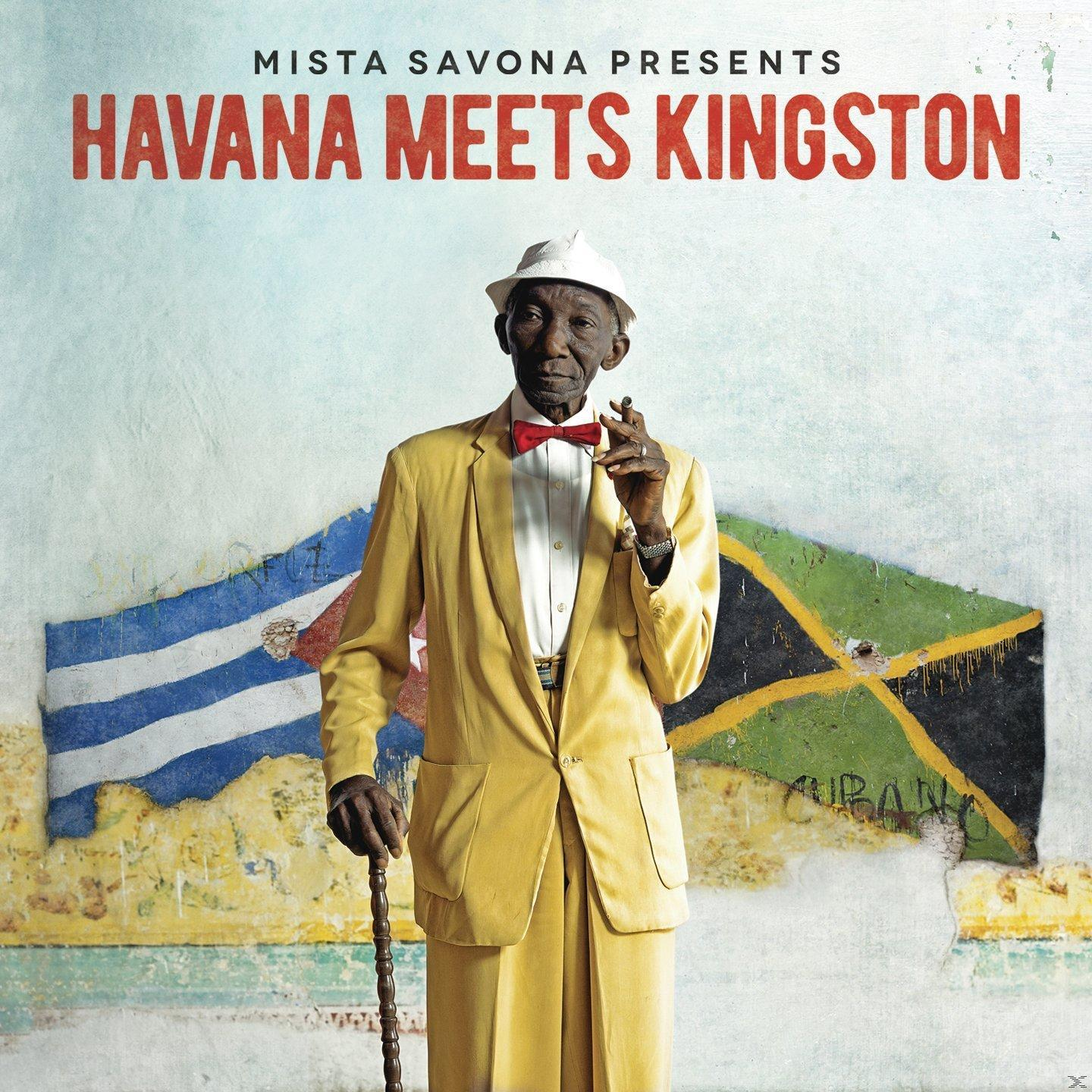 Mann in gelbem Anzug, der einen Stock hält und raucht, vor kubanischen und jamaikanischen Flaggen.