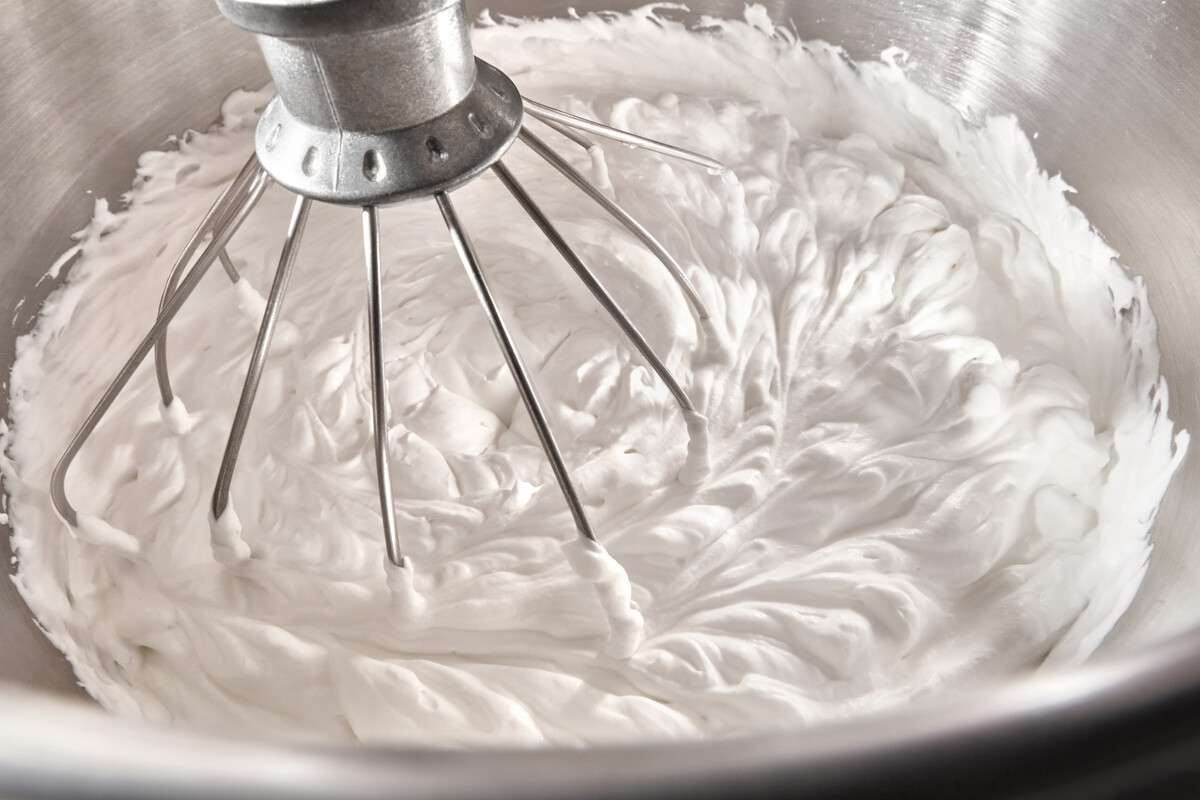 Eine Metallschüssel mit Schlagsahne, die von einem Schneebesen verrührt wird.