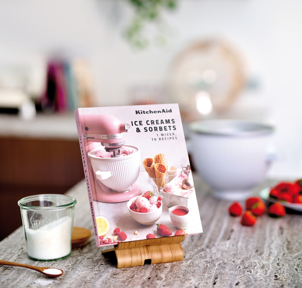 KitchenAid-Eiscreme-Buch auf einem Ständer. Ein rosa KitchenAid-Mixer und Zutaten sind in der Nähe.