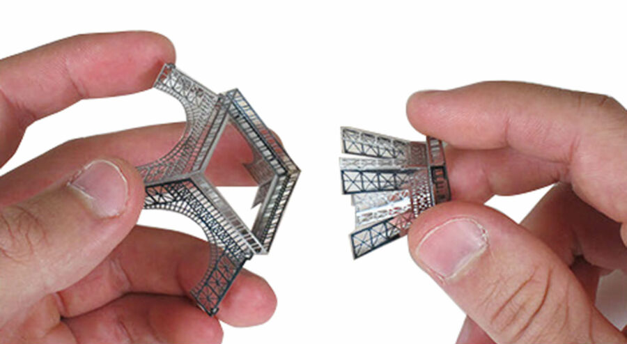 Kéz, amint összeállít egy ezüst fém Eiffel-torony modellt.