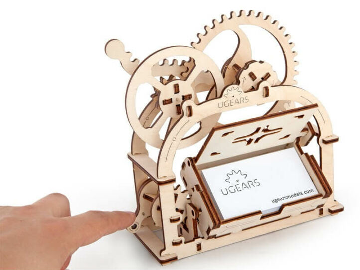 Egy fa UGEARS névjegykártyatartó, egy kézzel a mechanizmussal való interakcióval.