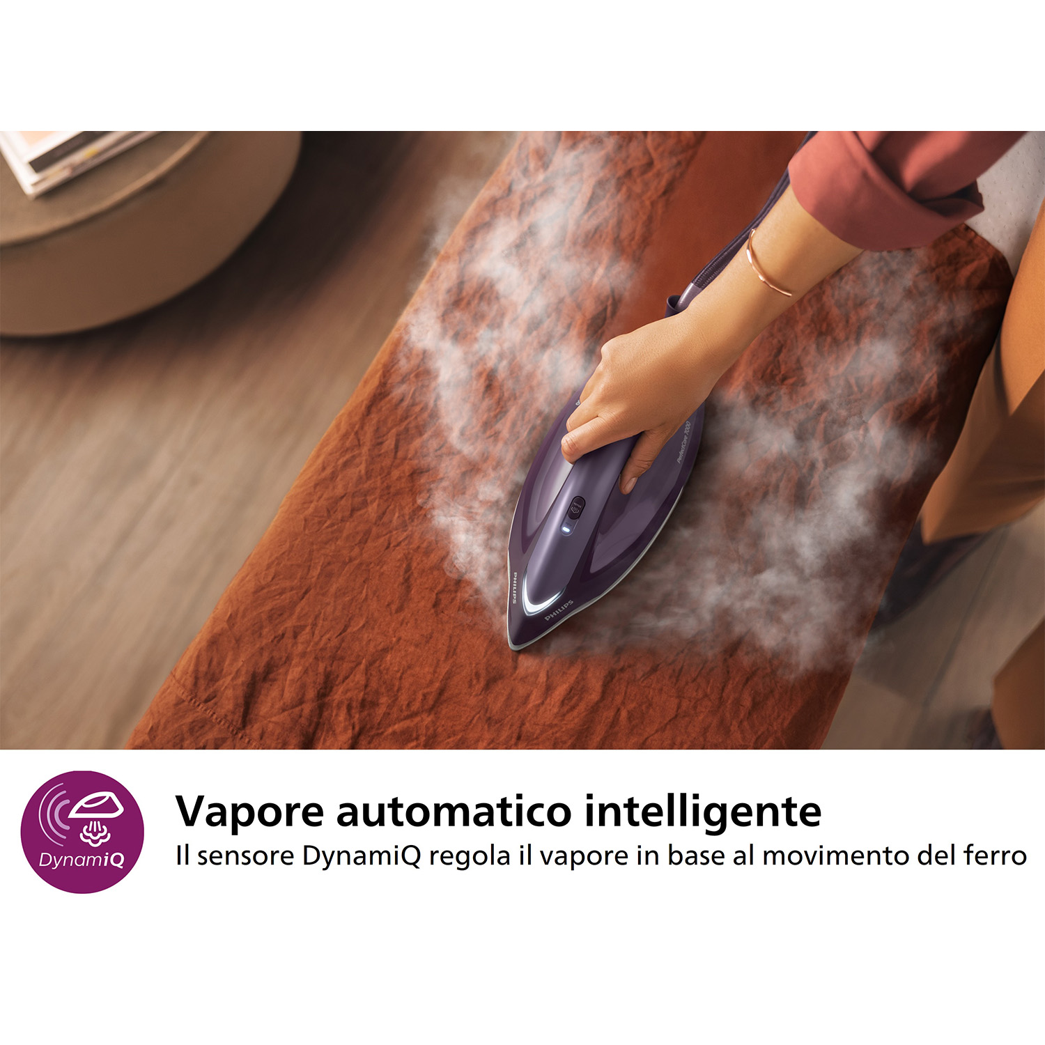 Asse da stiro con vapore che esce da un ferro da stiro viola, una mano lo tiene.