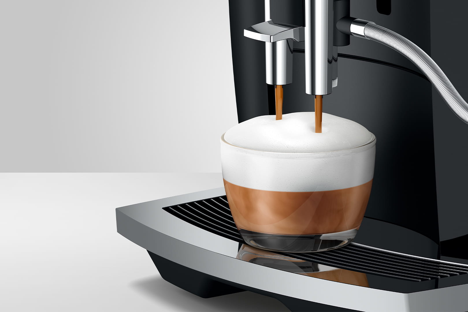 Primer plano de una cafetera dispensando un capuchino. La taza está llena de café y cubierta con espuma.