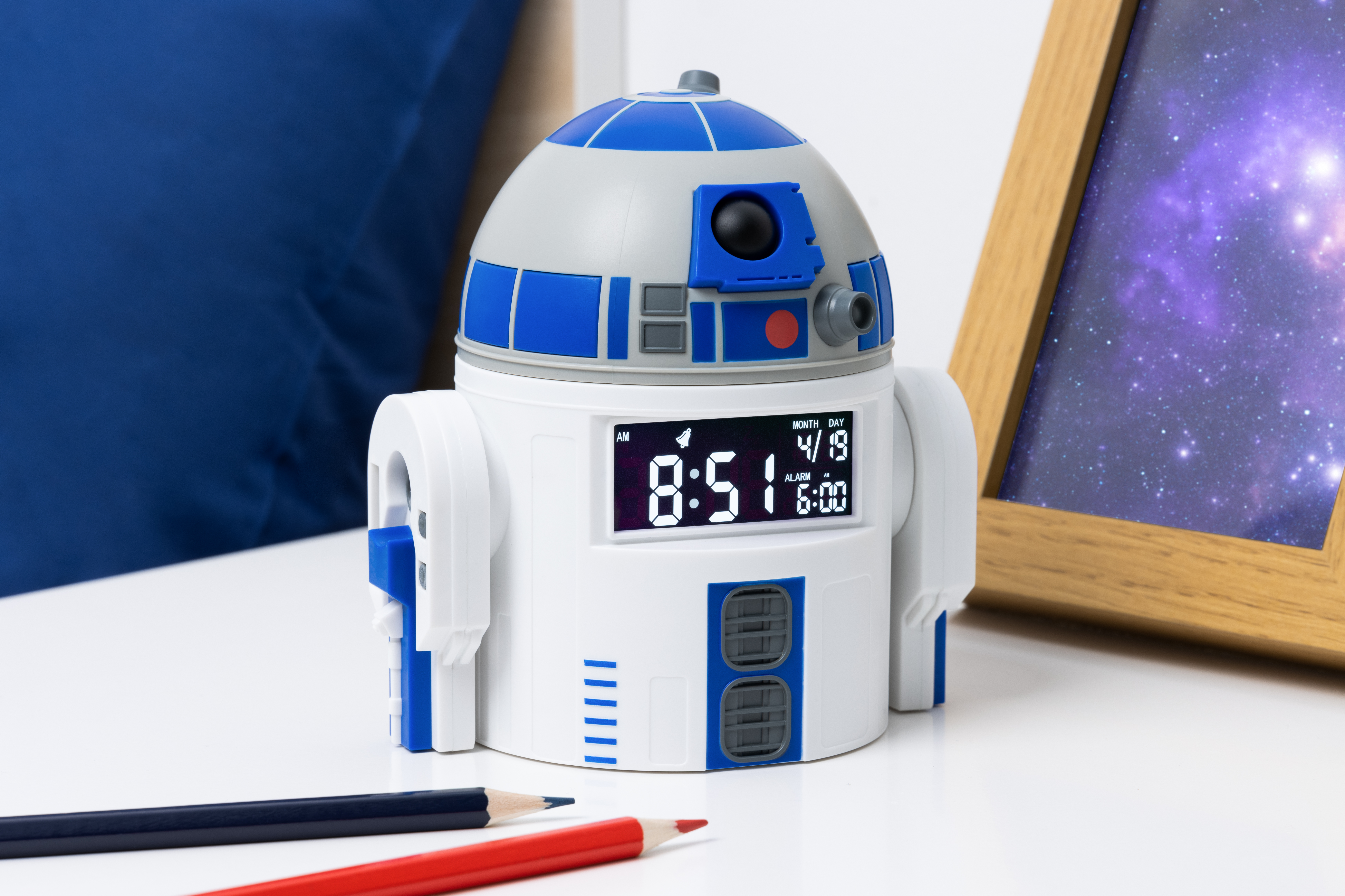 R2-D2 Wecker auf weißer Oberfläche mit Stiften und einem gerahmten Bild.