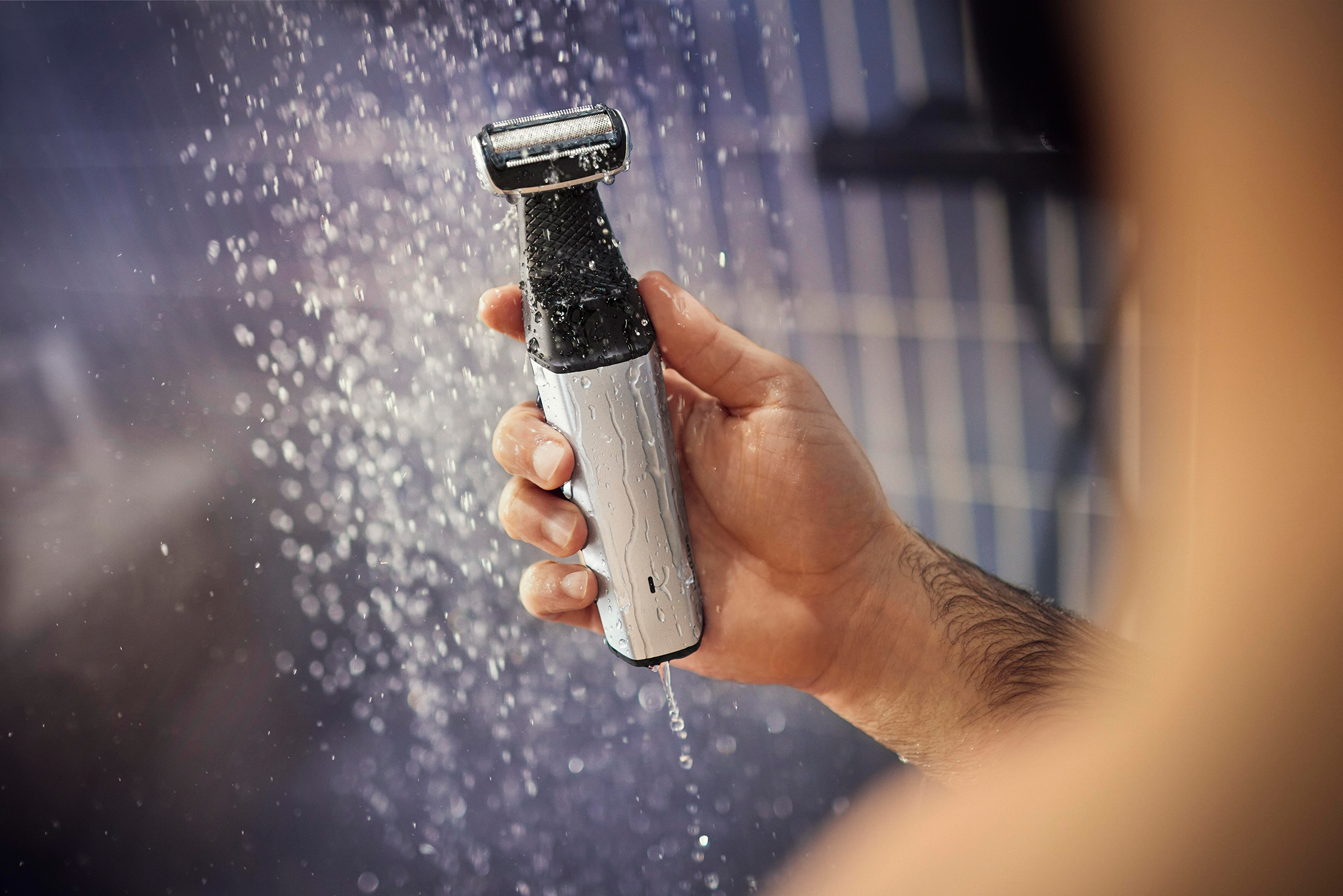 Een persoon die een zilveren en zwarte bodygroomer vasthoudt met water dat eromheen spat.