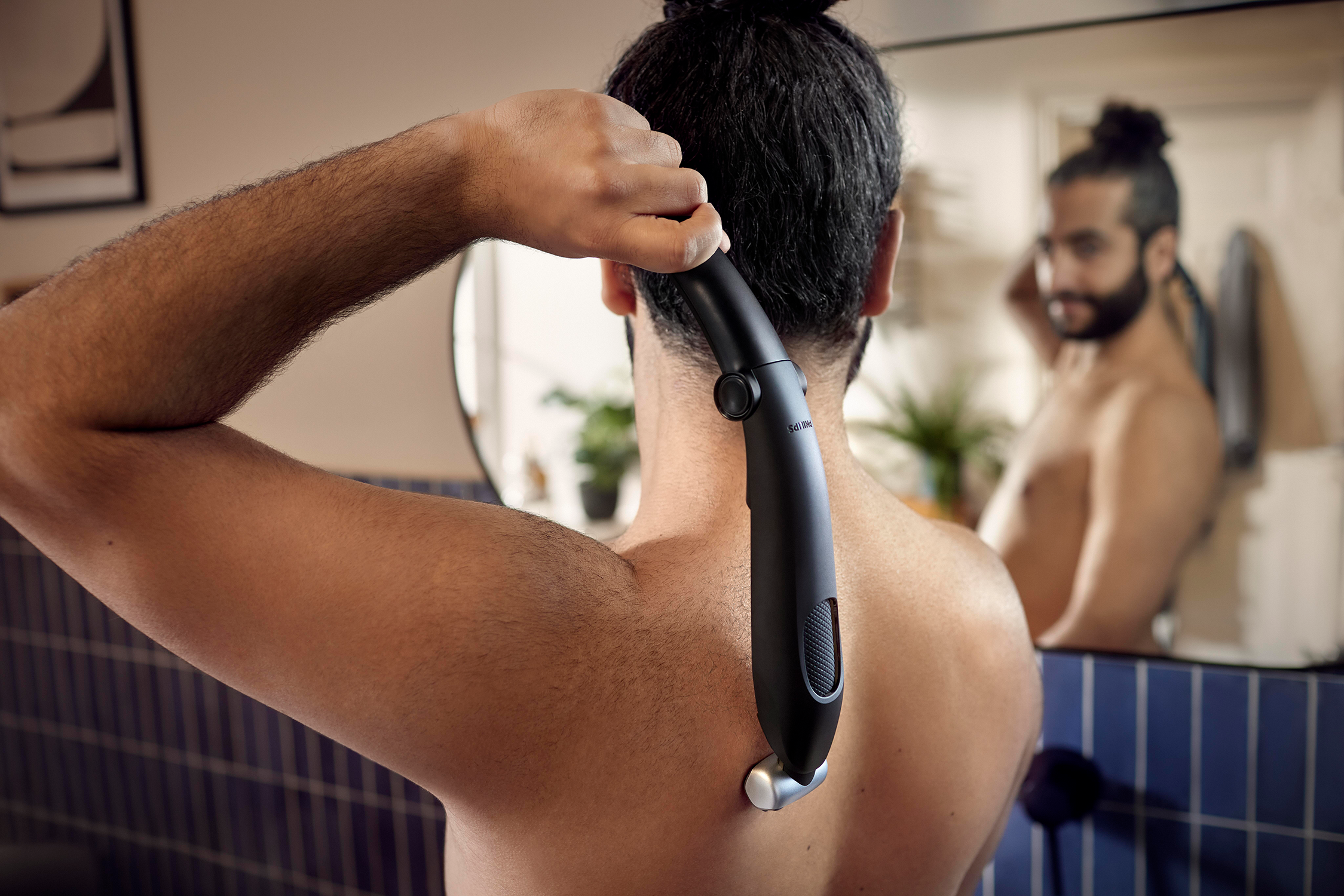 Een man scheert zijn rug met een zwarte Philips trimmer voor een spiegel. Een andere man wordt weerspiegeld.