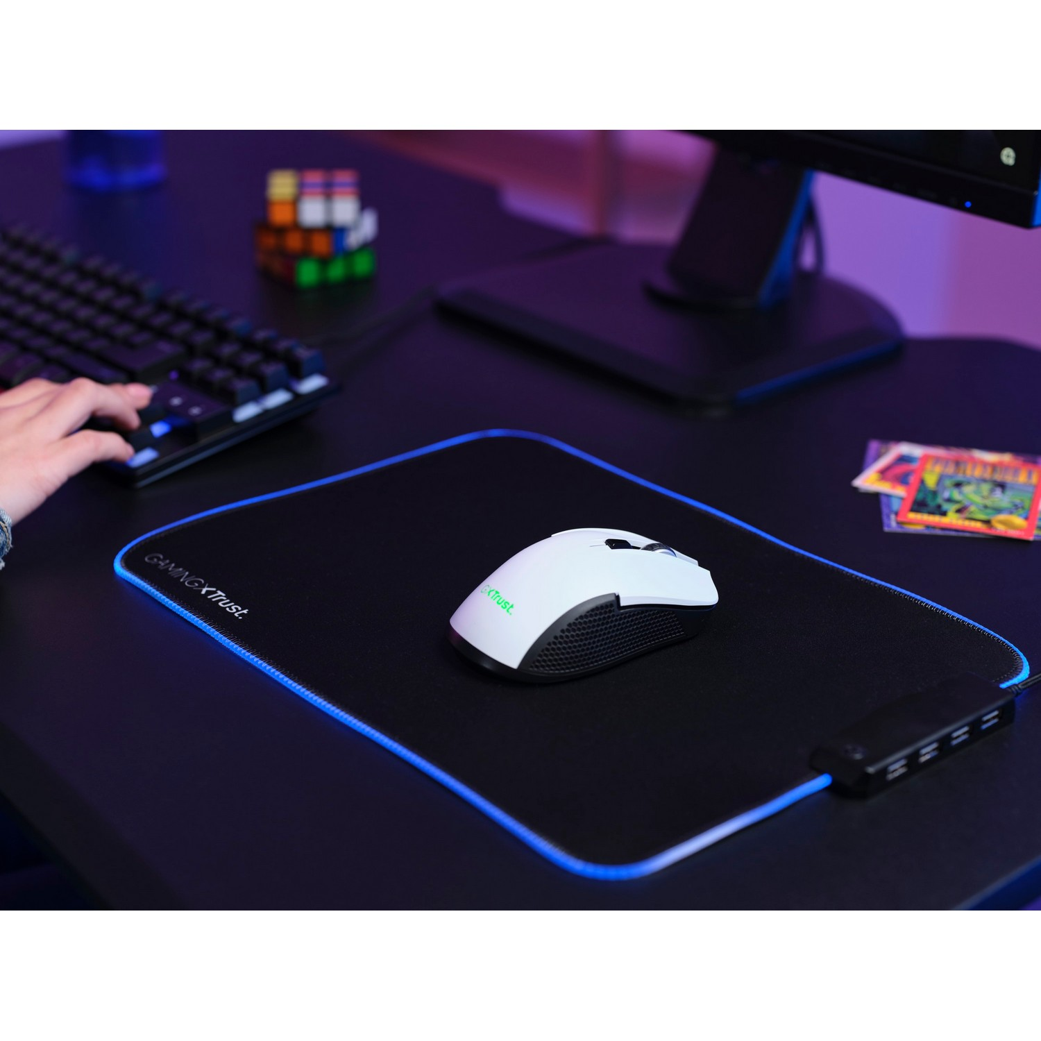 A white gaming mouse on a black mousepad with blue LED edging, next to a keyboard.
