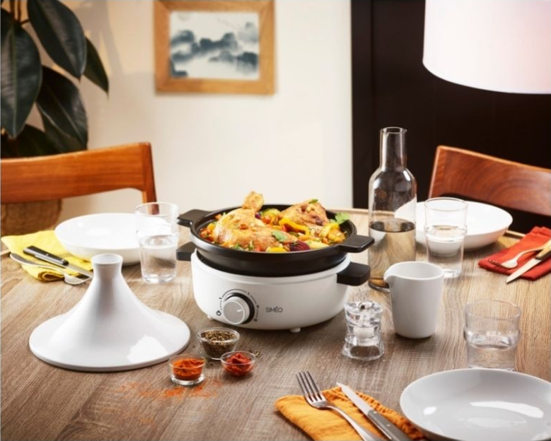 Dining table setting with cooked food in a white electric cooking device.